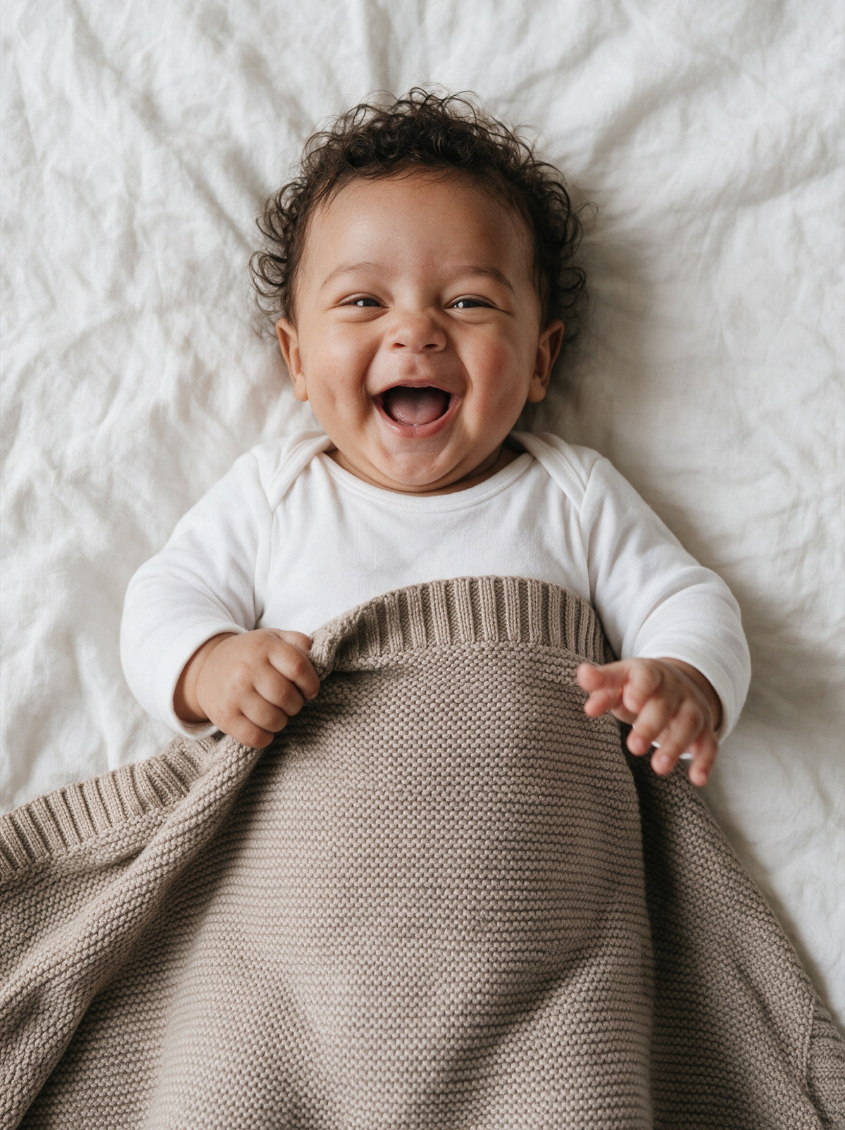 Laughing baby lying under a Truffle knitted blanket